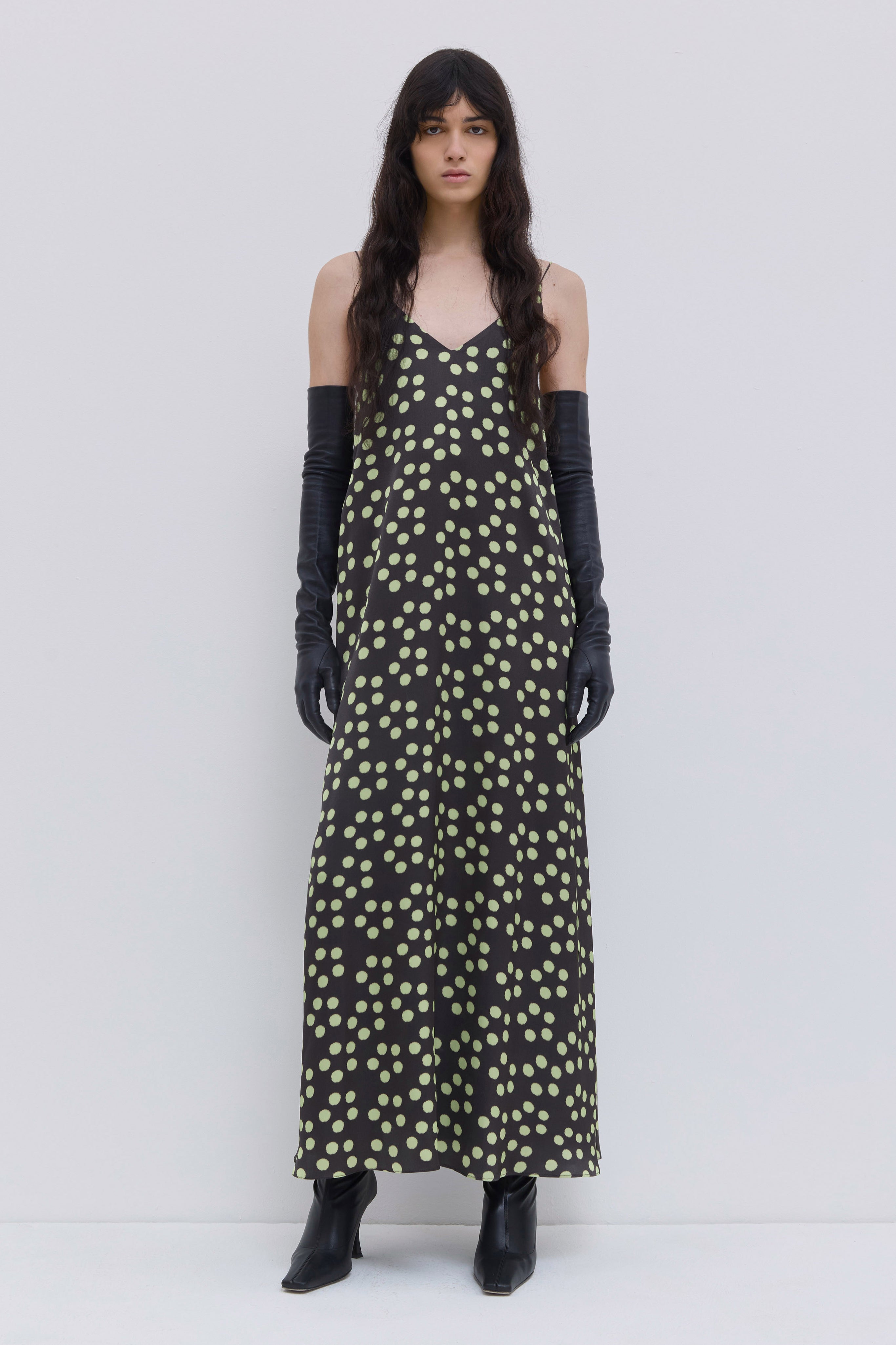 Model wearing a dark forest penny print A-line maxi dress with thin straps, V-neckline and scattered dot pattern by Christian Wijnants