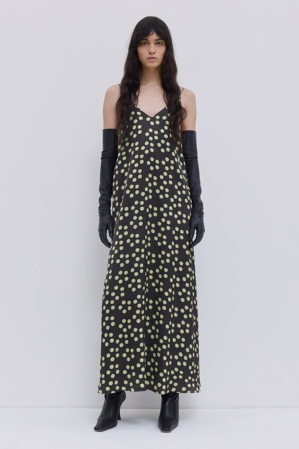 Model wearing a dark forest penny print A-line maxi dress with thin straps, V-neckline and scattered dot pattern by Christian Wijnants