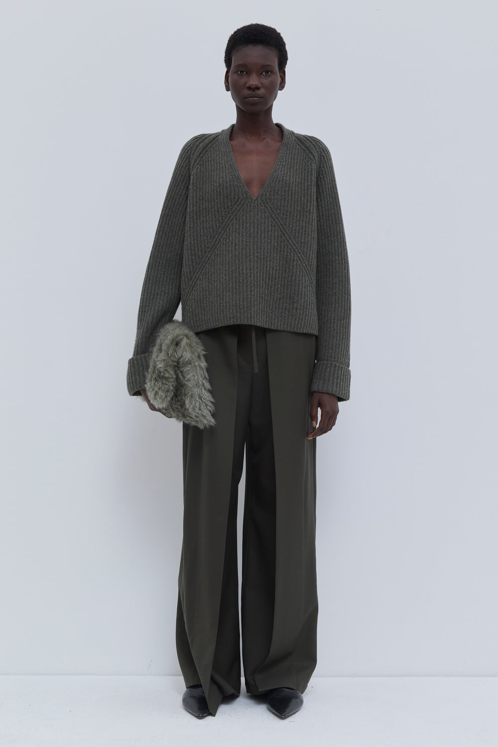 Model wearing a forest melange ribbed merino wool and cashmere V-neck sweater with wide-leg tailored trousers.